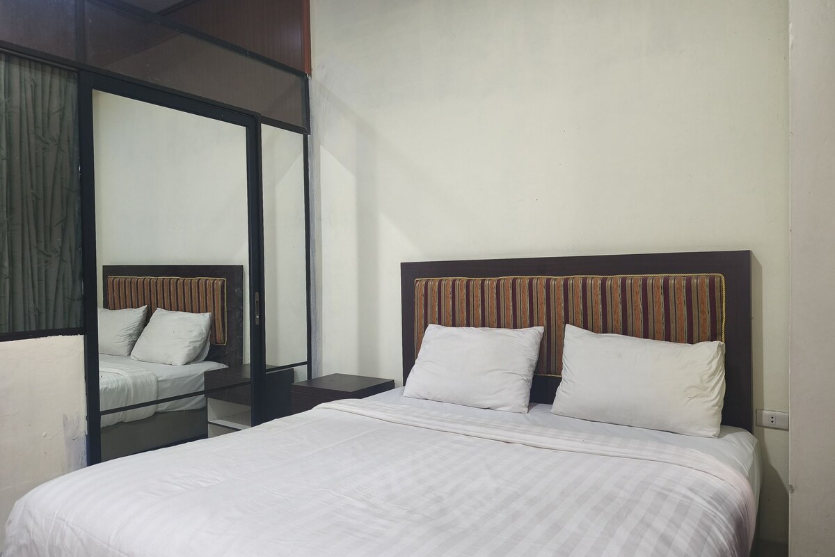 A hotel room with a bed, a nightstand, a mirror, and a window.
