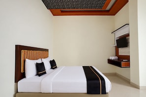 Habitación de hotel con cama, cabecera, televisor de pantalla plana y un pequeño estante con toallas.