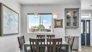 A dining area with a table and chairs, a window with a view, a clock, and a cabinet with decorative items.