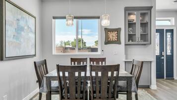 A dining area with a table and chairs, a window with a view, a clock, and a cabinet with decorative items.