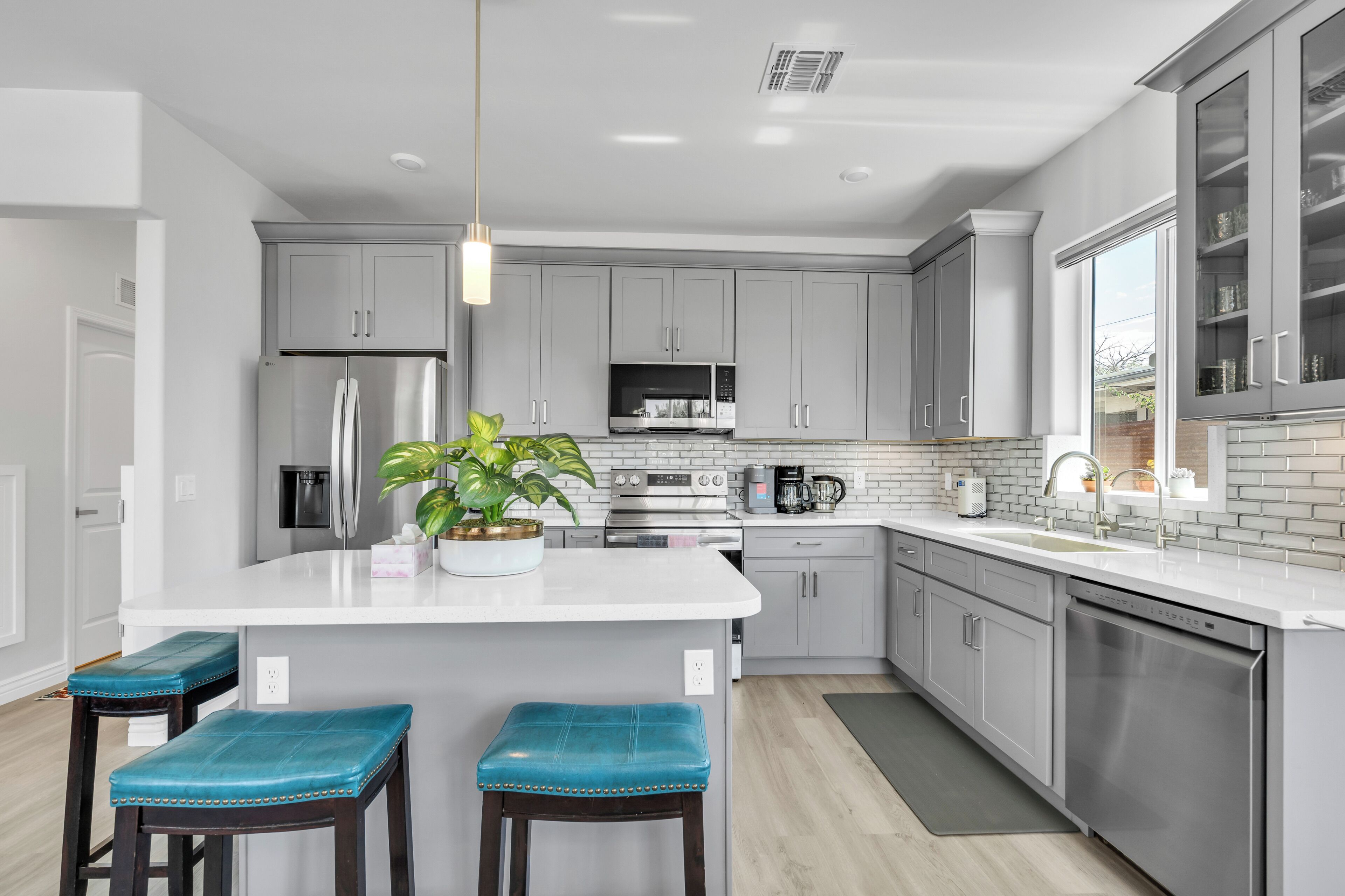 A modern kitchen with grey cabinets, a central island with bar stools, a built-in oven, and a large window.