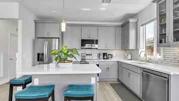 A modern kitchen with grey cabinets, a central island with bar stools, a built-in oven, and a large window.