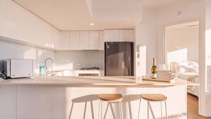 Een moderne keuken met witte kastjes, een roestvrijstalen koelkast, een ingebouwde gasoven en een groot kookeiland met barkrukken.