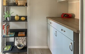 Una cocina con encimera de madera, un altavoz rojo y estanterías con libros y utensilios de cocina.