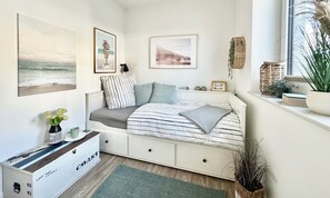 Ein Schlafzimmer mit einem Bett, einem Schminktisch, einem Fenster mit Pflanzen und Bildern an der Wand.