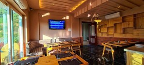 Restaurante com televisão exibindo uma partida esportiva, mobiliário de madeira e vista para o verde lá fora.