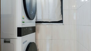 Un área de lavandería con lavadora, secadora y un pequeño contenedor para guardar objetos, con botellas.