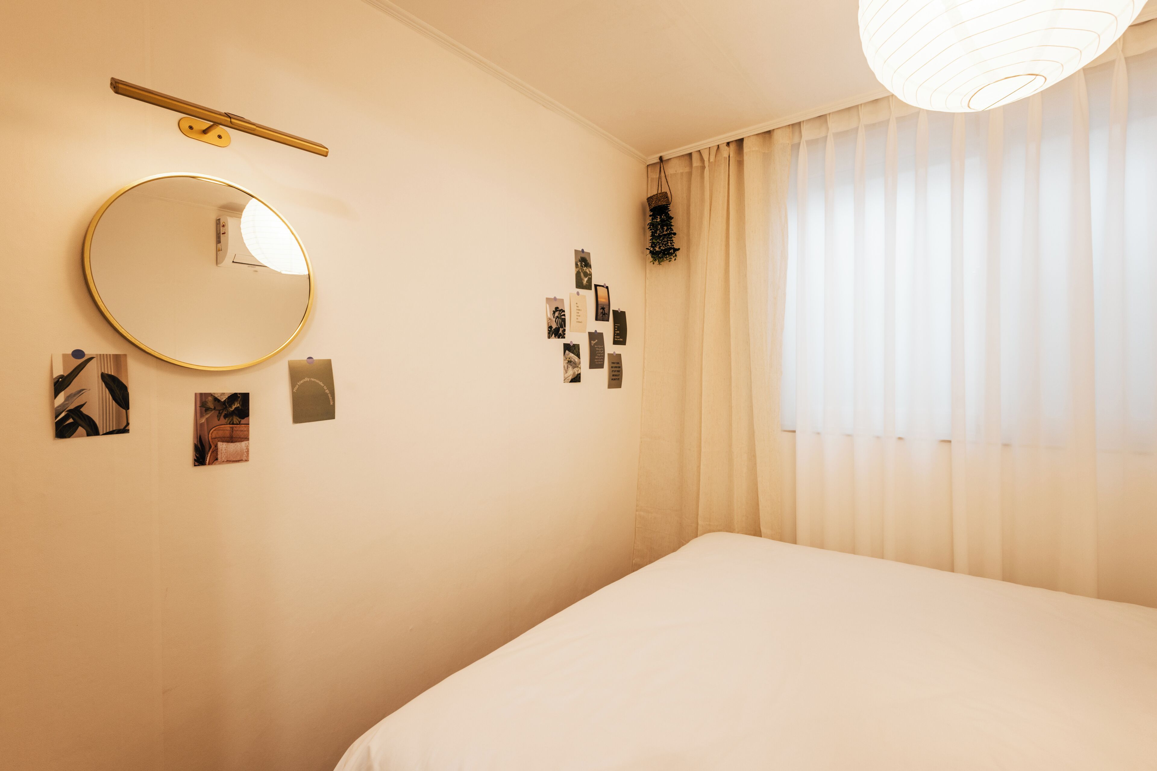 A bedroom with a bed, a round mirror, a wall-mounted shelf, and a window with curtains.