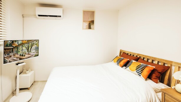 Habitación de hotel con una cama, televisor montado en la pared, un ventanal pequeño y una mesita de noche.