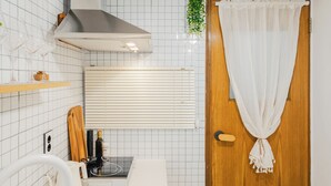Una cocina con un lavamanos de acero inoxidable, una puerta de madera con cortina blanca y una lámpara en el techo.