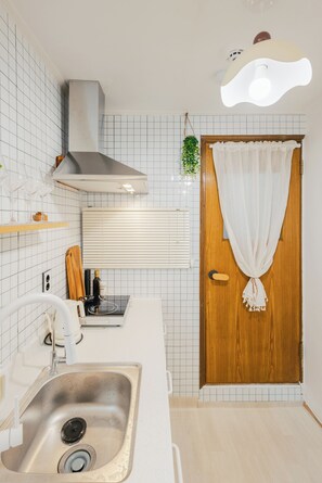 Eine Küche mit einem Edelstahl-Spülbecken, einer Holztür mit weißem Vorhang und einer Deckenleuchte.