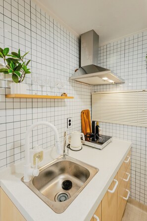 Eine Küche mit Spüle aus Edelstahl, weiß gefliestem Spritzschutz, Holzschränken, einer weißen Arbeitsplatte und einer Dunstabzugshaube.