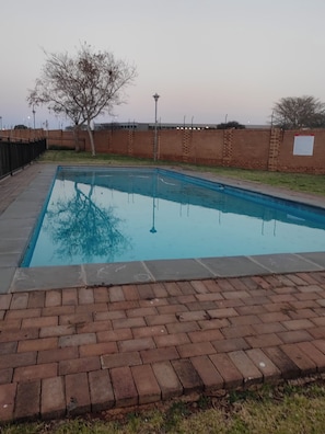 A rectangular swimming pool with a brick border, surrounded by a brick wall and a grassy area.
