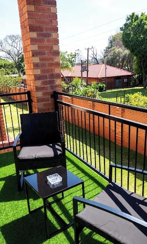 A balcony with a brick pillar, a wicker chair, a small table, and a metal railing.