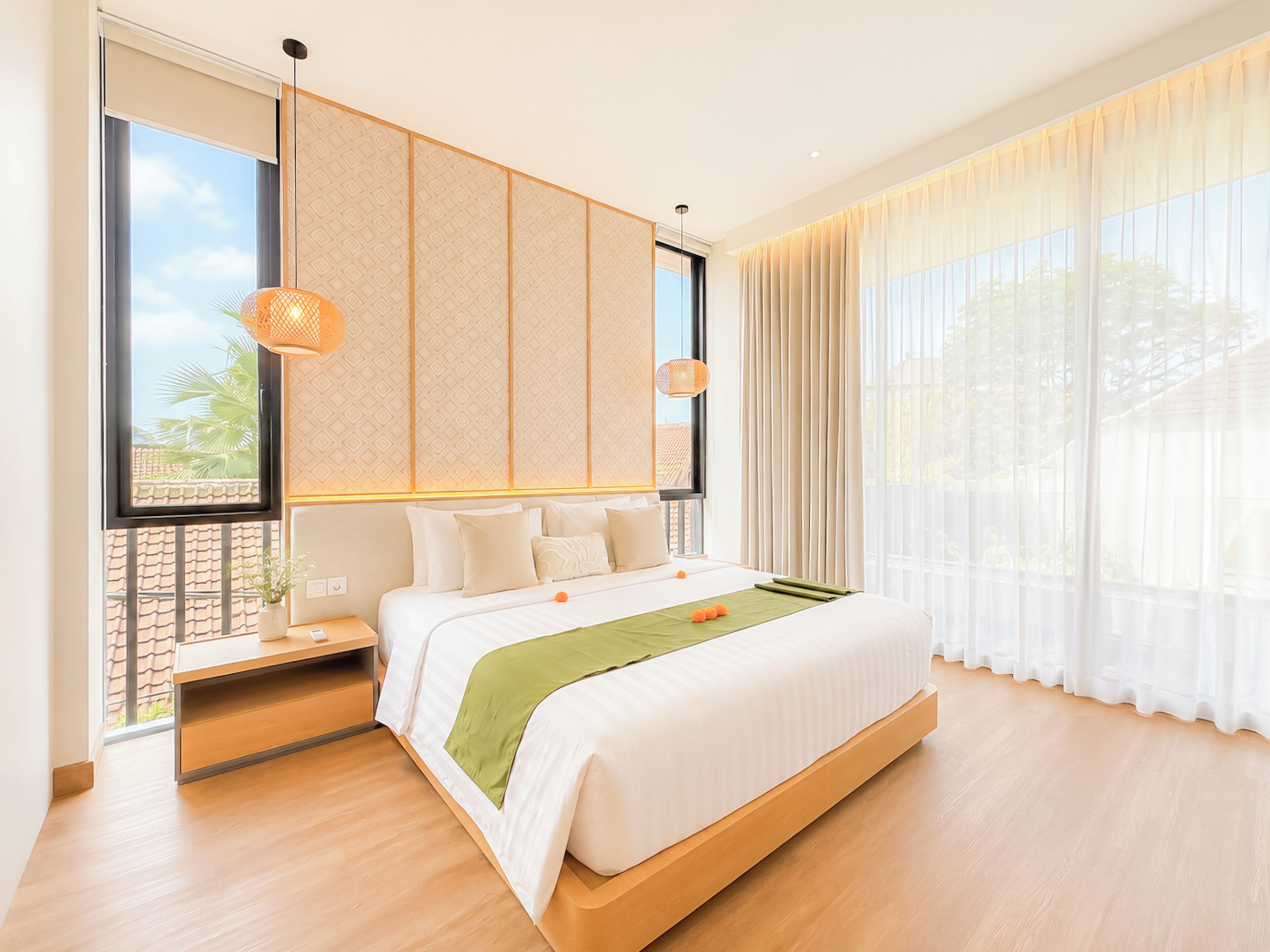 A modern hotel room with a large bed, a bedside table, a window with a view, and a hanging light fixture.
