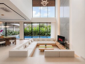 Un saló modern amb un sofà modular, una televisió de pantalla plana i vista a una piscina.