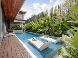 A modern outdoor pool area with a wooden deck, two lounge chairs, and lush tropical plants. - Alaya Villa Seminyak by Nagisa Bali (Badung)