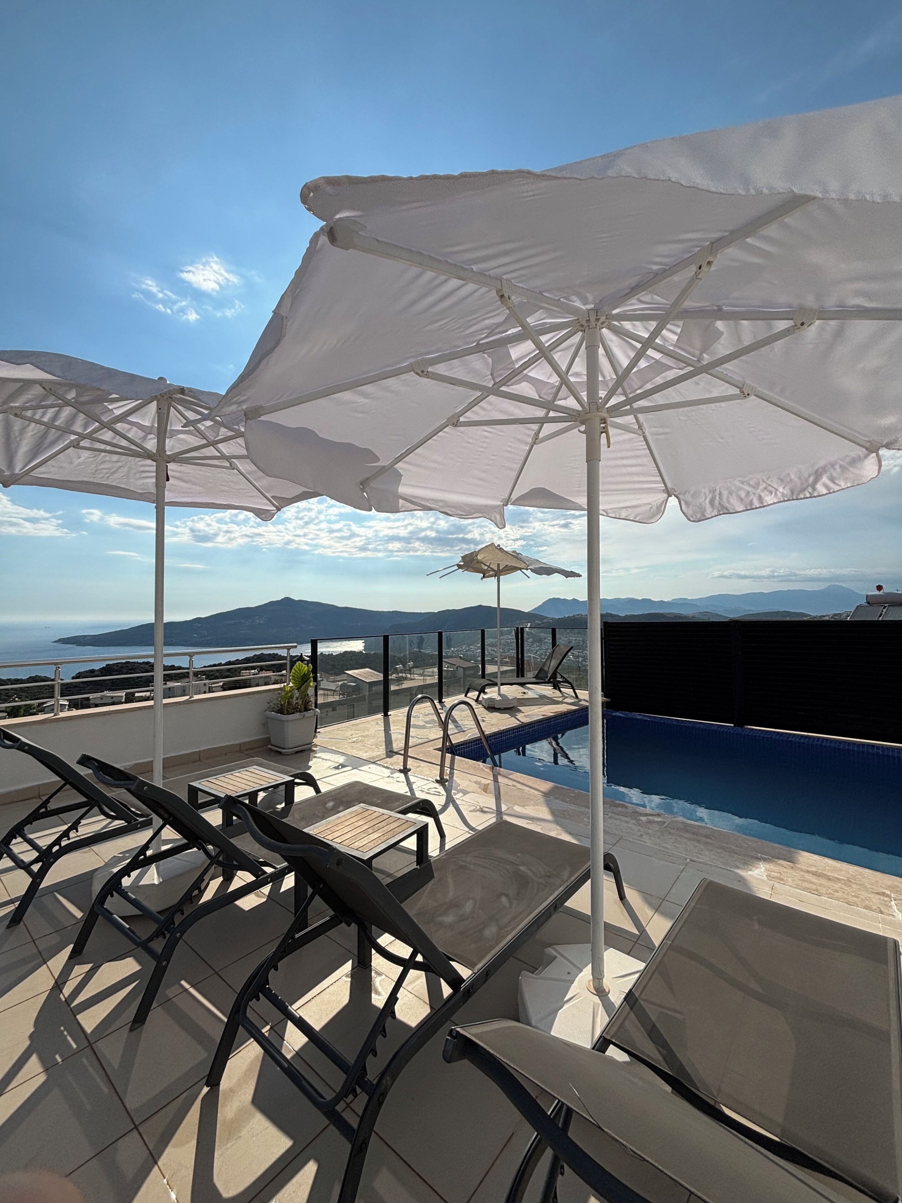 A rooftop terrace with a pool, lounge chairs, and umbrellas.