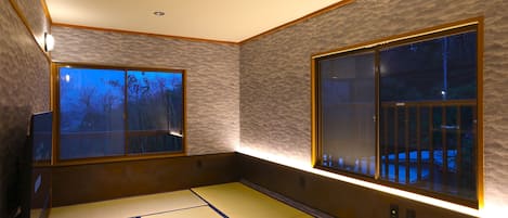 A traditional tatami mat room with two large windows and a wall-mounted light fixture.