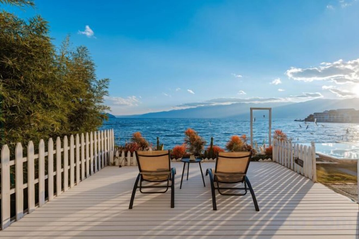 A wooden deck with two chairs and a table, overlooking a body of water with a clear sky.
