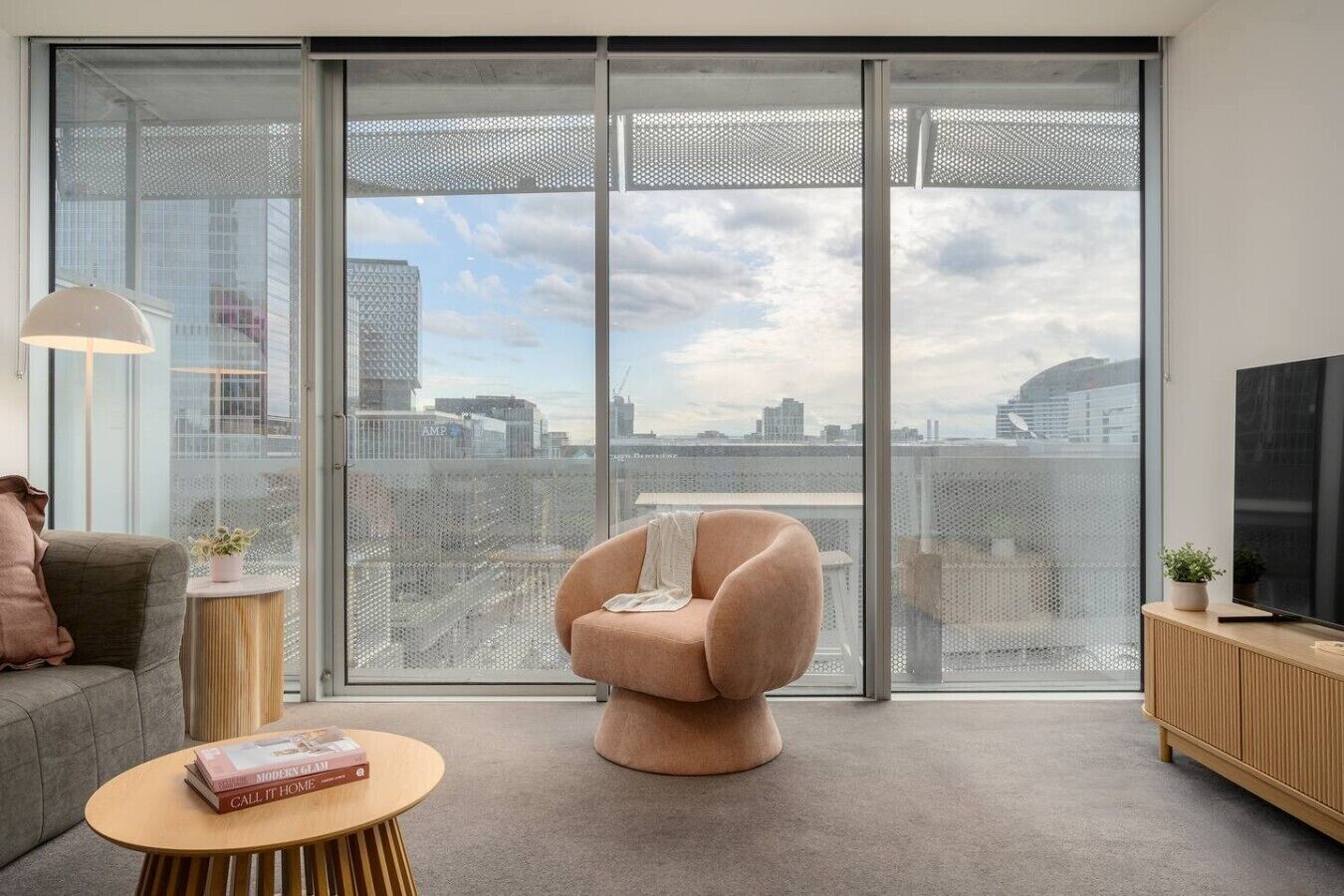 Ein modernes Wohnzimmer mit großem Fenster, einer Couch, einem Sessel, einem Couchtisch und einem Fernseher.