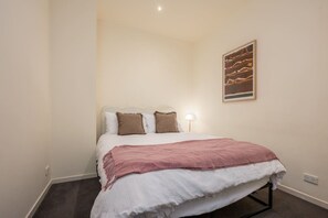A single bed with a white and pink bedspread, two pillows, a bedside lamp, and a framed artwork on the wall. - Downtown Stylish Apartment w/ Pool, Gym & Parking! (West Melbourne)