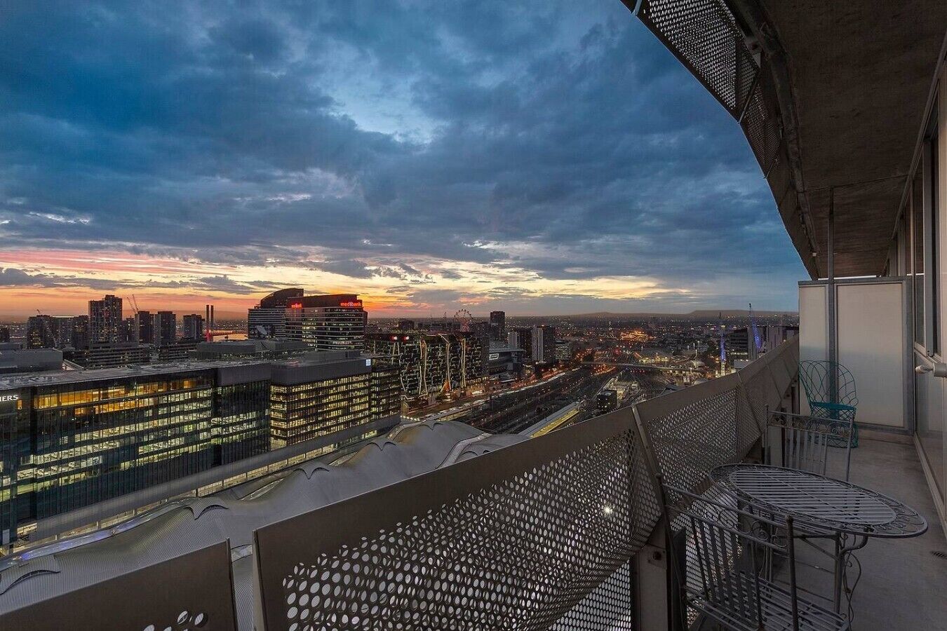 A cityscape view from a balcony with a metal railing and a table.