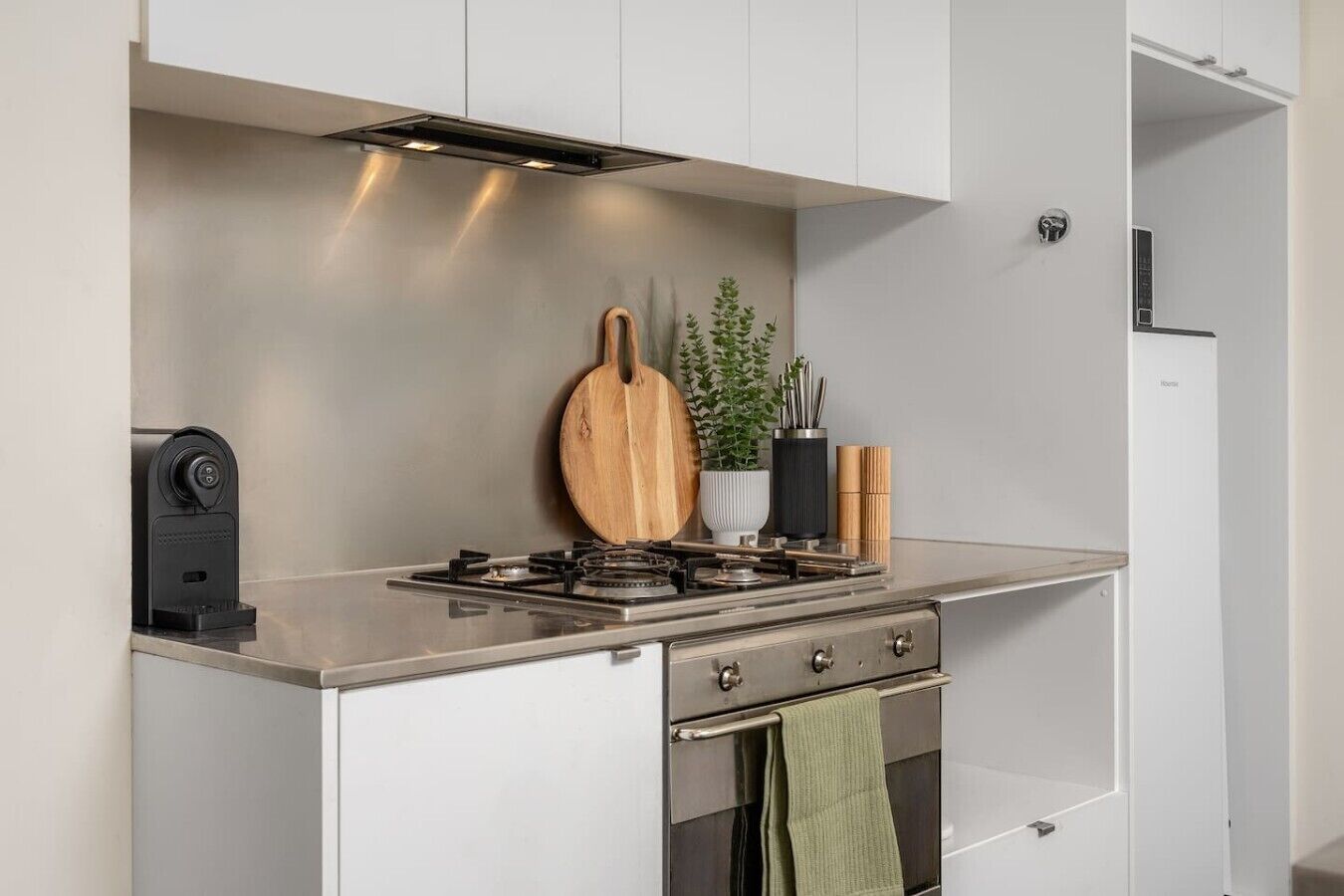 Une petite cuisine équipée d’une cuisinière à gaz, d’une planche à découper en bois, d’une plante en pot et d’une serviette accrochée à la porte du four.