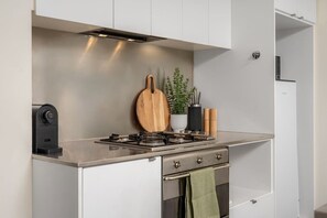 A compact kitchen with a gas stove, a wooden cutting board, a potted plant, and a towel hanging on the oven door. - Downtown Stylish Apartment w/ Pool, Gym & Parking! (West Melbourne)