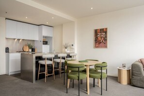 A modern kitchen with white cabinets, a central island with stools, and a dining area with green upholstered chairs. - Downtown Stylish Apartment w/ Pool, Gym & Parking! (West Melbourne)