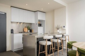 A modern kitchen with a central island, bar stools, and a dining table. - Downtown Stylish Apartment w/ Pool, Gym & Parking! (West Melbourne)