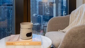 Une chambre moderne avec une grande fenêtre, une petite table d’appoint ronde en bois, un fauteuil beige et un livre intitulé « Élégance simple ».