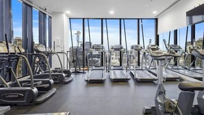 Une salle de sport équipée de tapis de course, de vélos elliptiques et d’appareils de musculation, avec de grandes fenêtres offrant une vue sur le paysage urbain.
