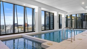 Une piscine intérieure moderne, dotée de grandes baies vitrées offrant une vue dégagée sur le paysage urbain.