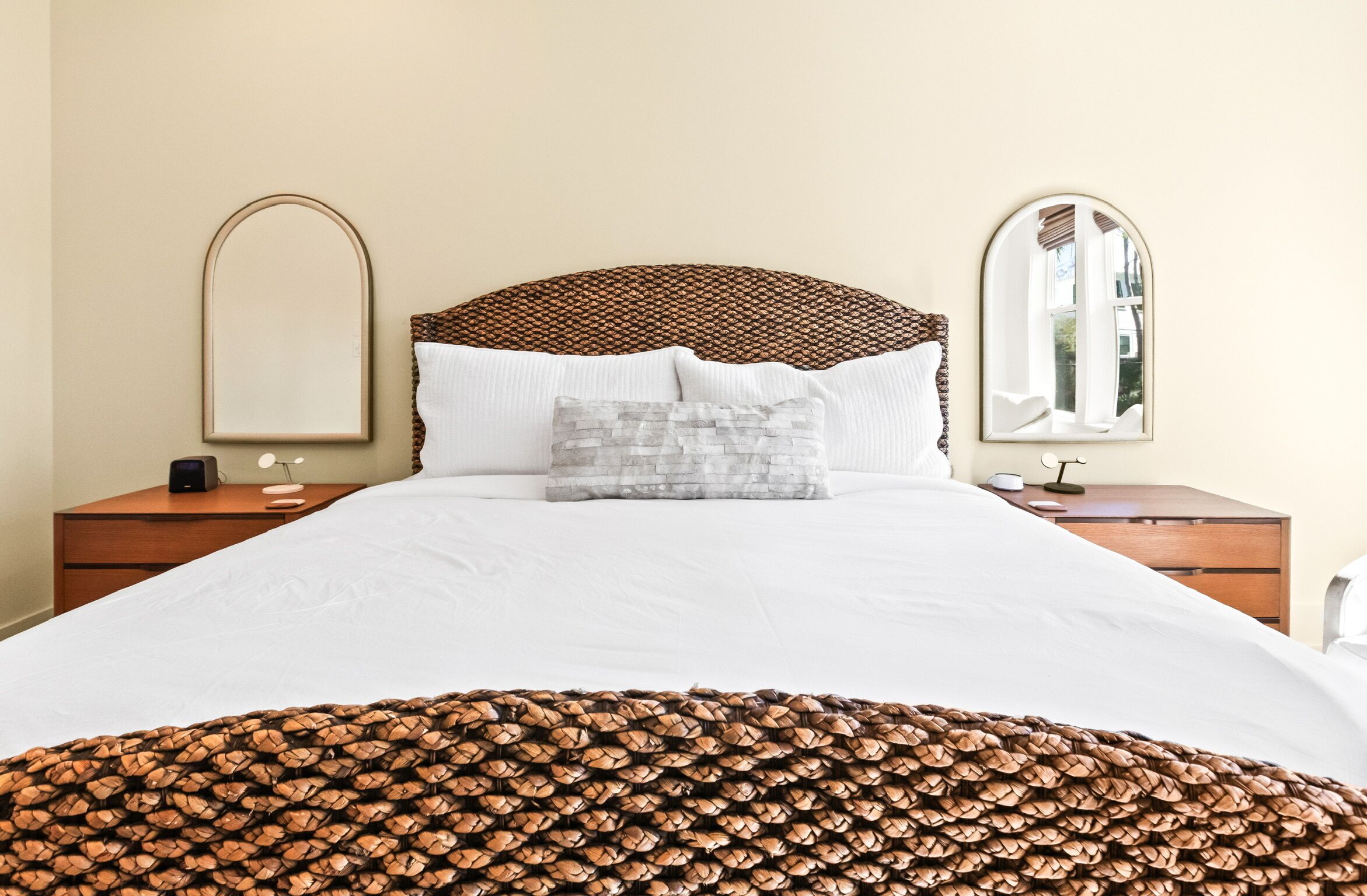 A hotel room with a large bed, two bedside tables, a nightstand, a mirror, and a window.