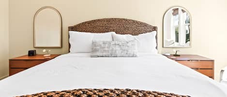 A hotel room with a large bed, two bedside tables, a nightstand, a mirror, and a window.