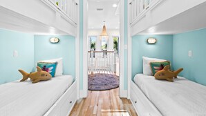 A corridor with two beds on either side, a wooden floor, and a view of the outside through a glass door. - Family Tides 30A | Seagrove Beach | Sleeps 16 | LSV Bikes | Pool  Carriage House (Santa Rosa Beach)