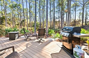 Una terraza al aire libre con una parrilla, asientos y vistas a un bosque.