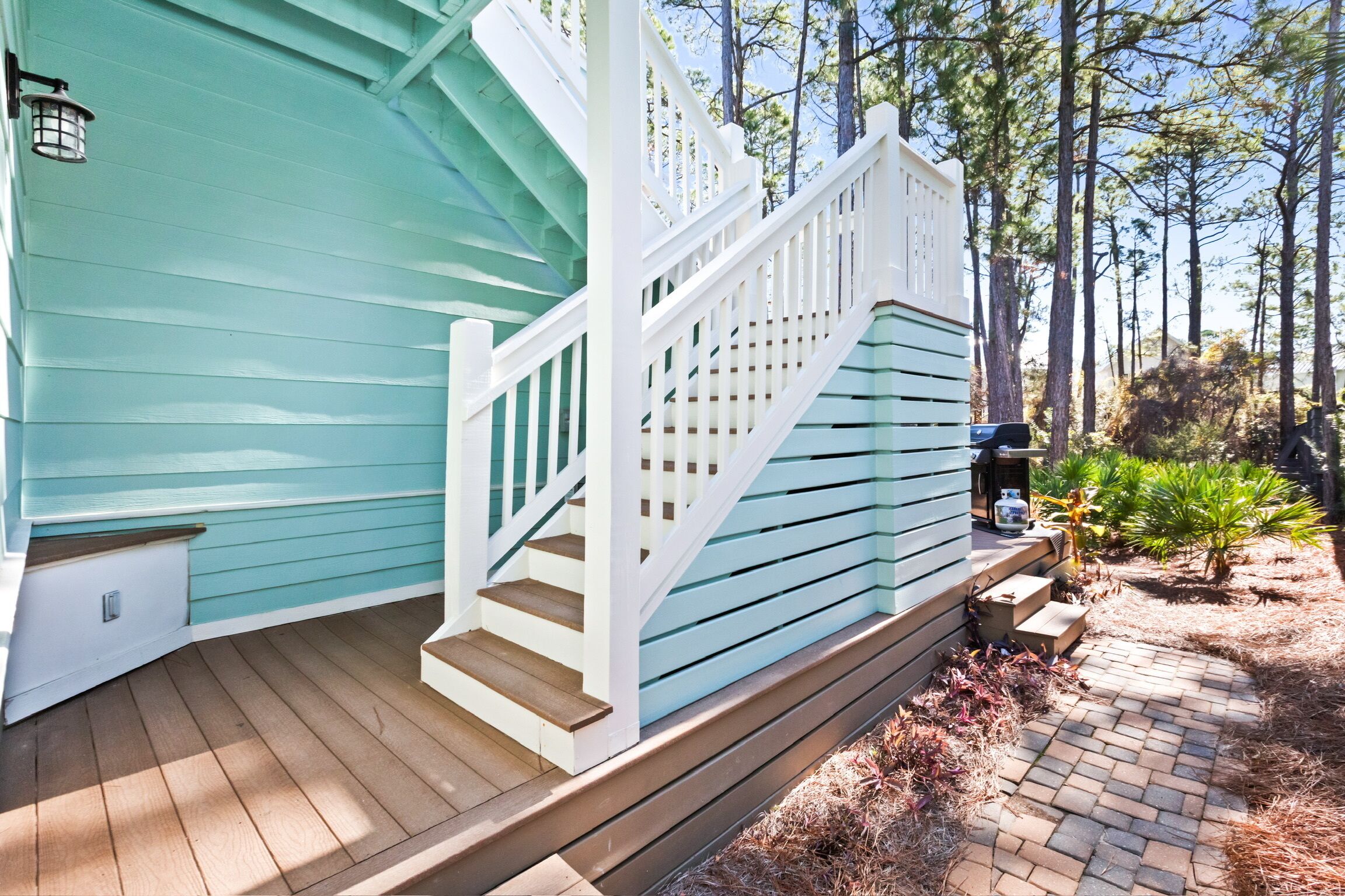A wooden deck with a staircase leading to a house with teal siding.