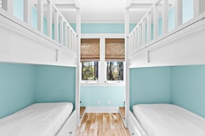 Una habitación con dos literas, una ventana con vistas a árboles y una pared azul claro.