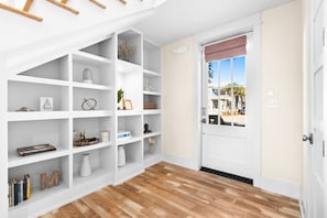 Un pasillo con un estante empotrado blanco, suelo de madera y una puerta que da al exterior.