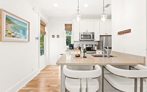 A modern kitchen with white cabinetry, a central island with bar stools, stainless steel appliances, and pendant lighting. - Family Tides 30A Seagrove | Pool | Sleeps 16 (Santa Rosa Beach)