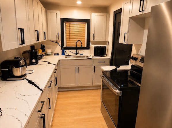 A compact kitchen with white cabinets, a microwave, a stove, and a coffee maker.