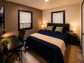 A hotel room with a bed, bedside tables, a desk, a chair, and a TV on the wall.