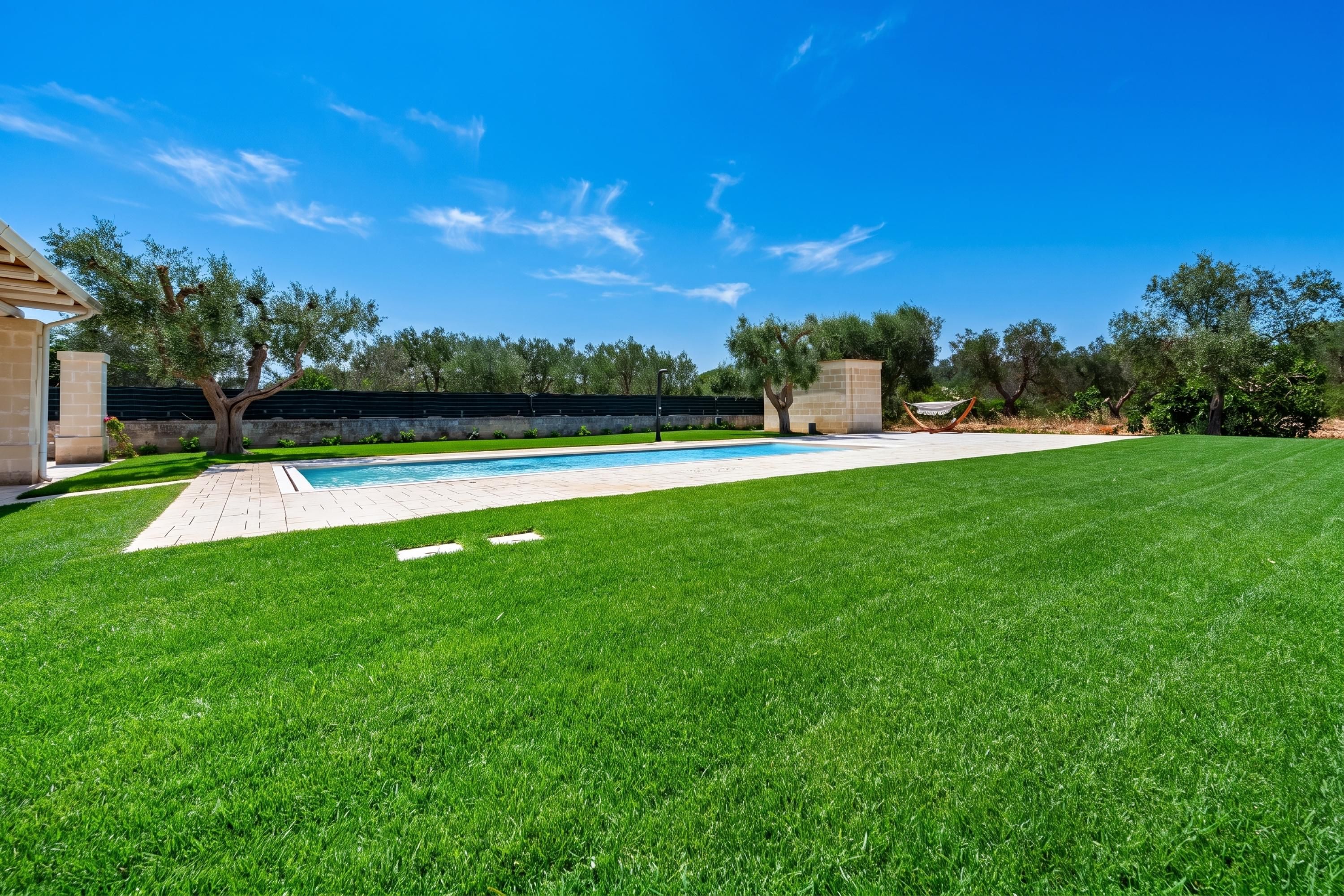 A well-maintained backyard with a swimming pool, a grassy lawn, and a stone wall.