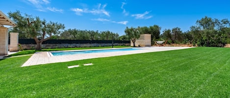 A well-maintained backyard with a swimming pool, a grassy lawn, and a stone wall.