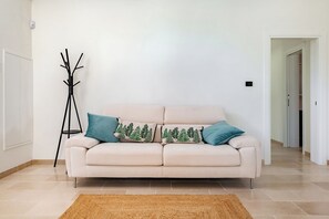 A beige sofa with two decorative pillows, a woven rug, and a black floor lamp in a room with white walls and a tiled floor. - Villa Fedali With Pool (Francavilla Fontana)