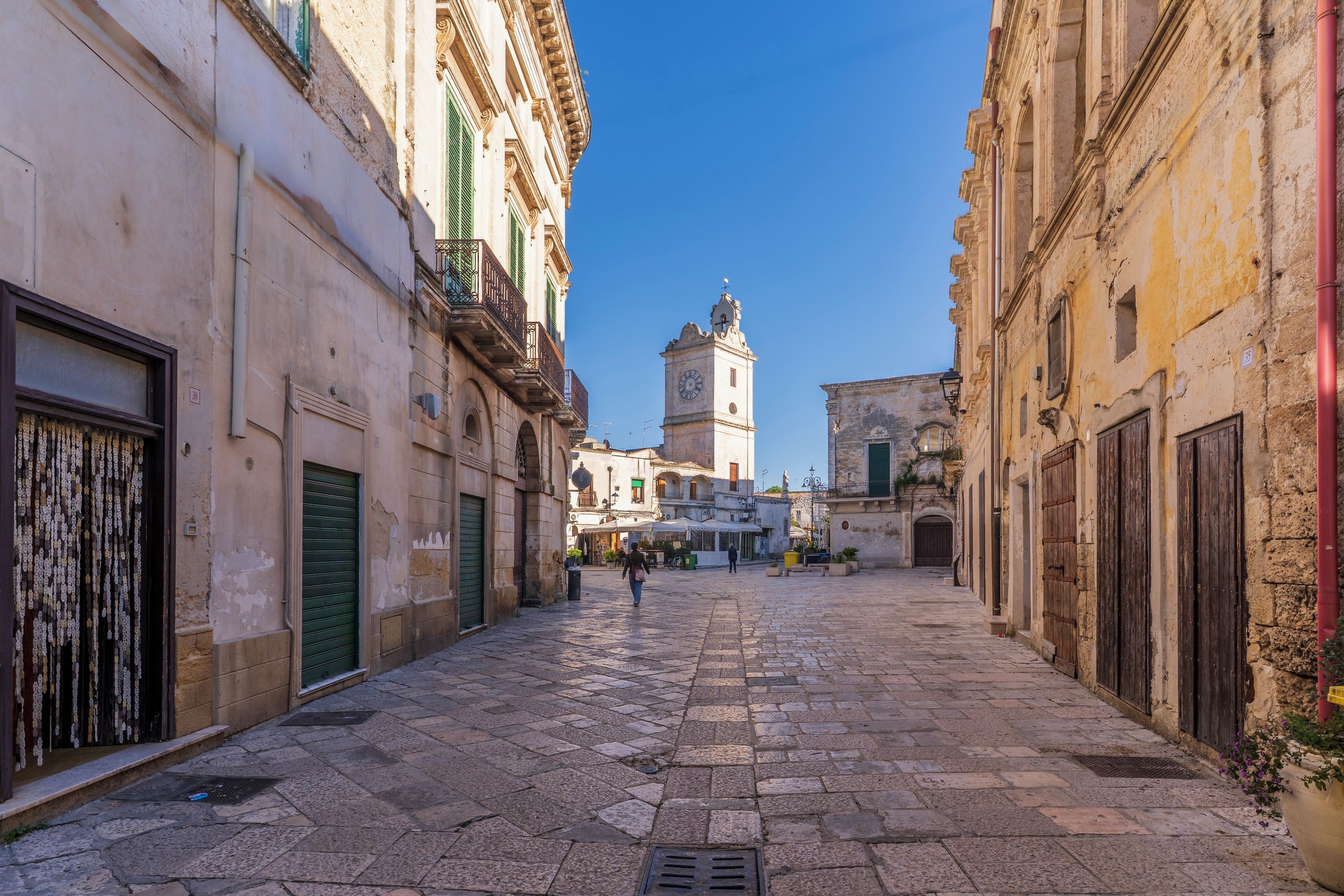 Una estrecha calle adoquinada flanqueada por edificios históricos, con una torre del reloj a lo lejos.