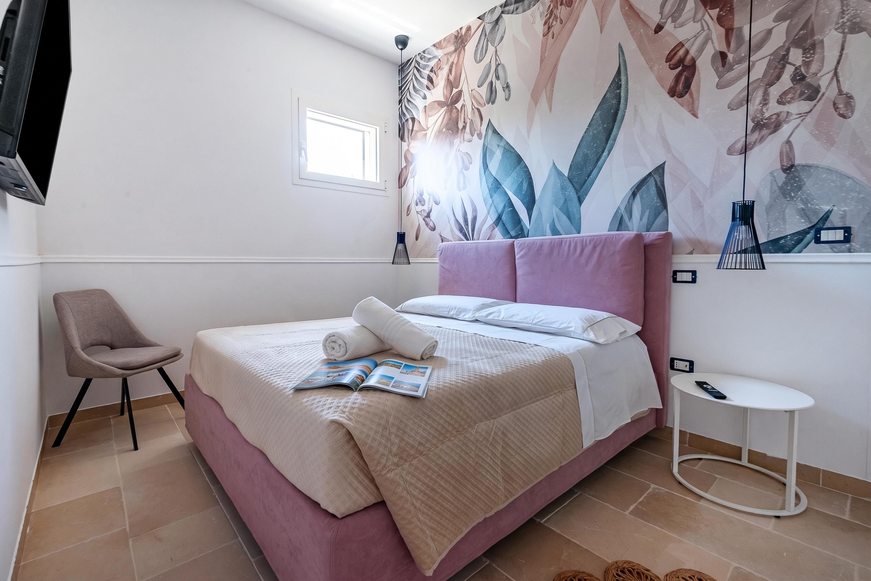 Une chambre à coucher avec un lit, une chaise, une petite table et un téléviseur fixé au mur.