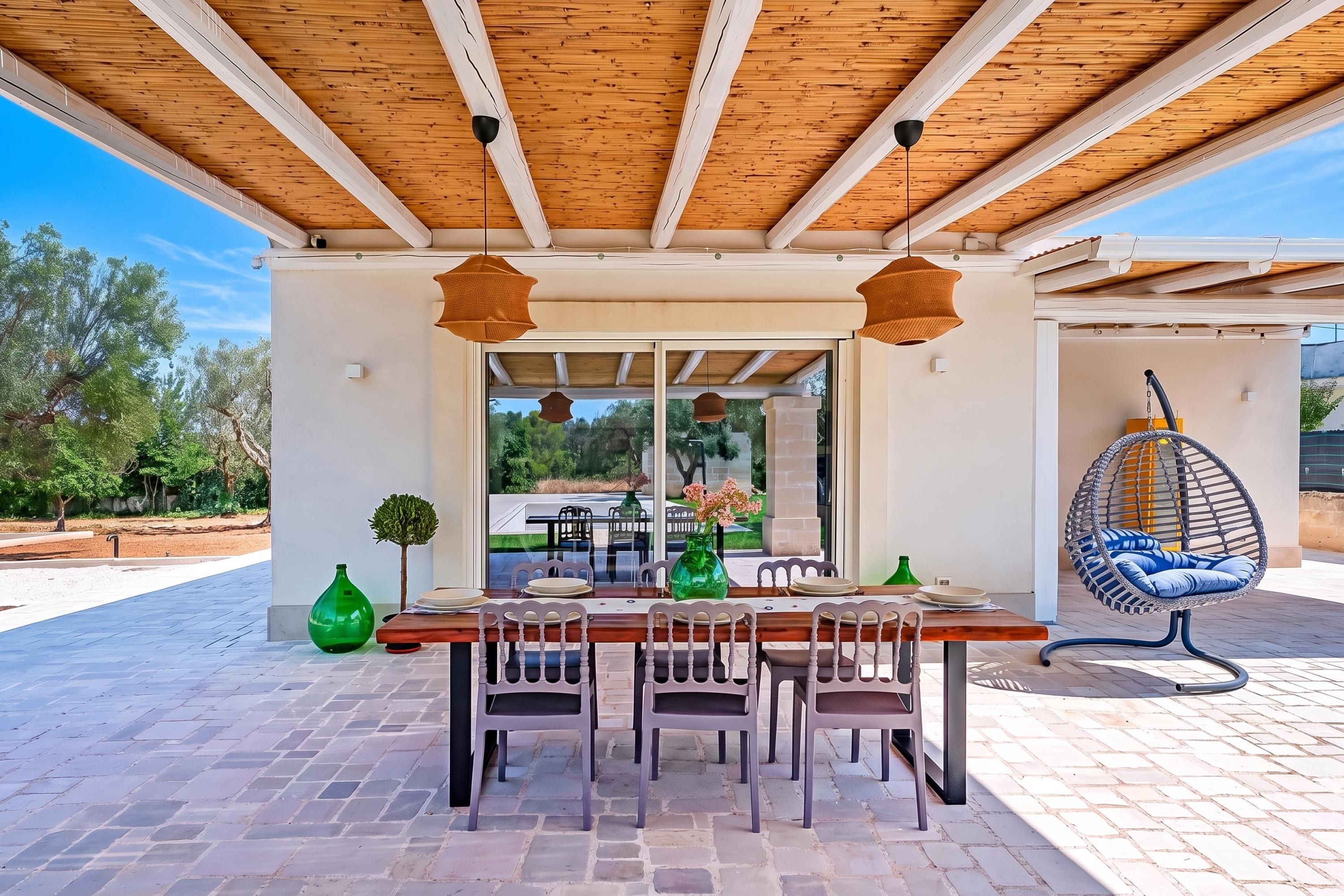 Un espace extérieur aménagé pour les repas, avec une pergola en bois, une table dressée pour quatre personnes et un fauteuil suspendu.